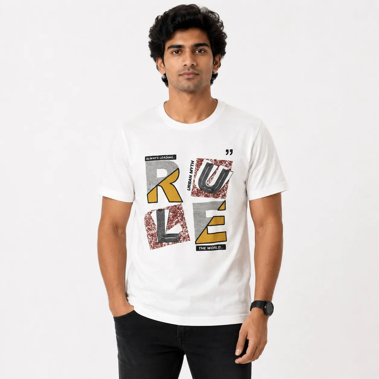 A man wearing a white short-sleeve graphic t-shirt with a stylized 'RULE' print in textured gray, black, and gold lettering, paired with black jeans against a plain white background.