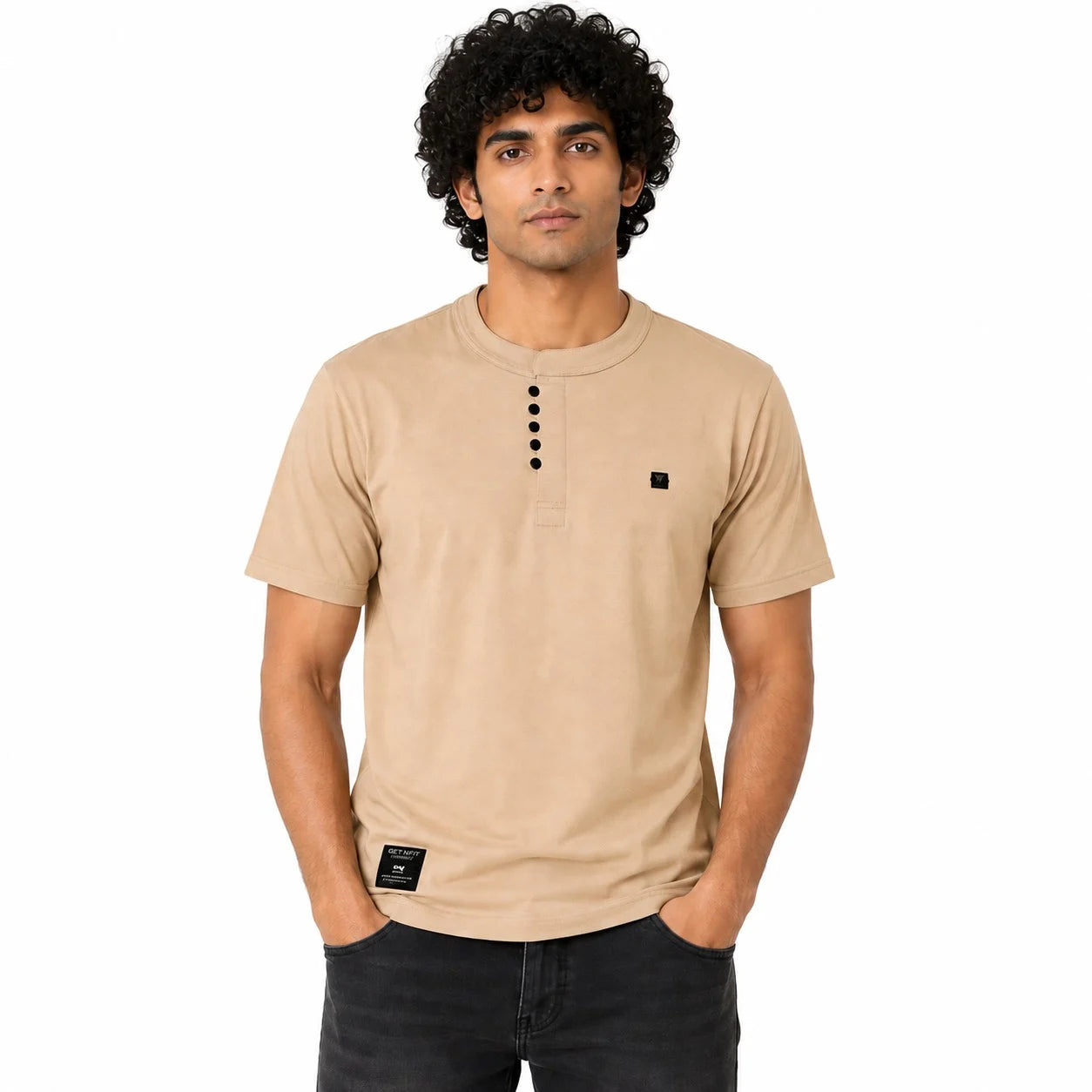 A man wearing a beige short-sleeve henley t-shirt with a black button placket and a small black square logo on the left chest, paired with dark jeans, against a plain white background.