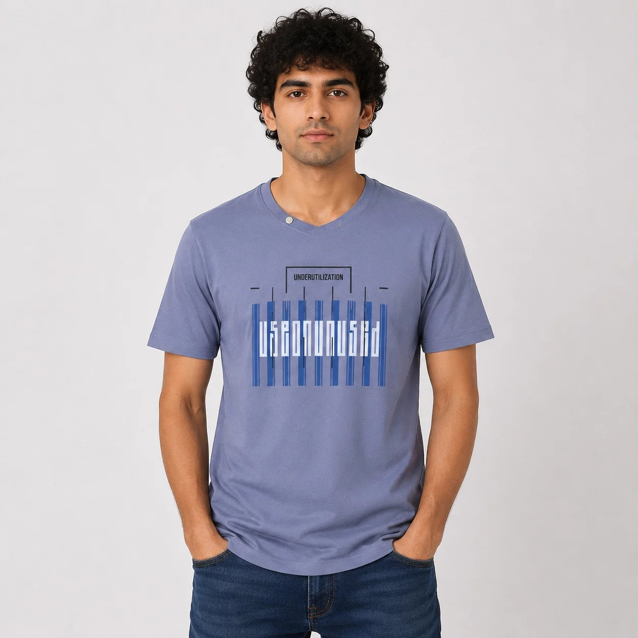 A man wearing a periwinkle blue t-shirt with a graphic print that reads 'UNIVERSITY OF DELHIA' in white and blue stripes, paired with dark blue jeans, against a light gray background.