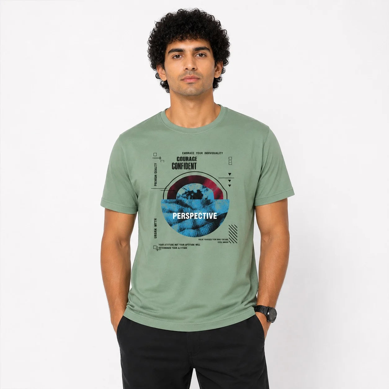A man wearing a sage green graphic t-shirt with a circular print that reads 'PERSPECTIVE' and 'CHOOSE CONFIDENCE', paired with black pants, standing against a plain white background.