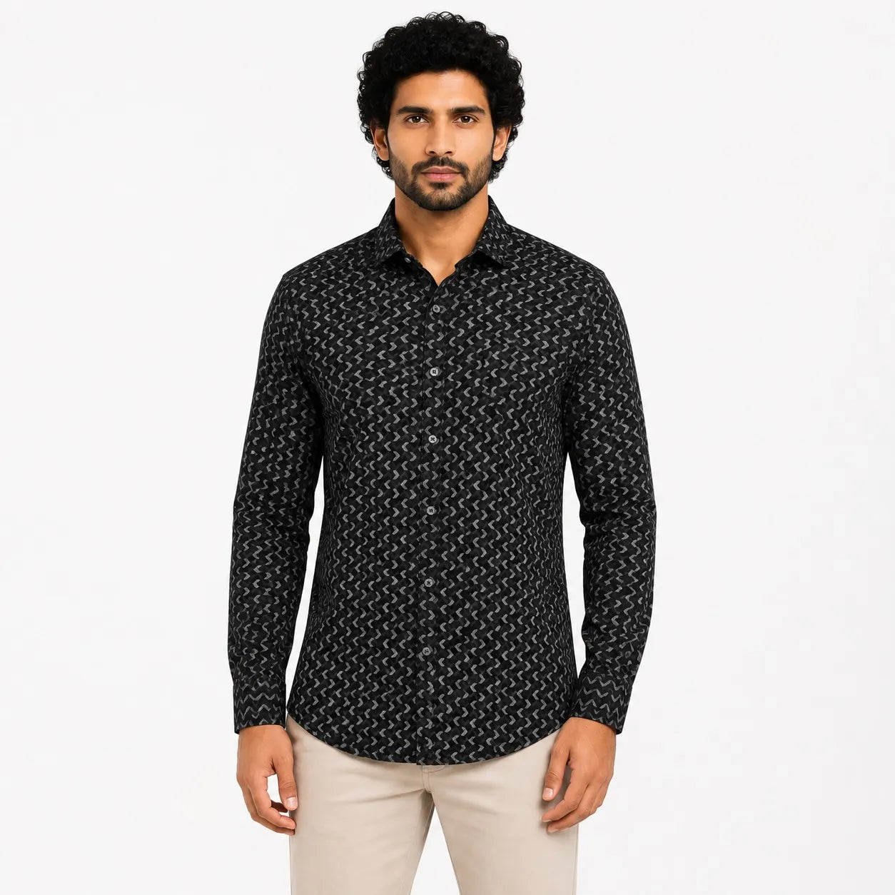 A man wearing a black long-sleeve button-up shirt with a white geometric pattern, paired with beige trousers, standing against a plain white background.