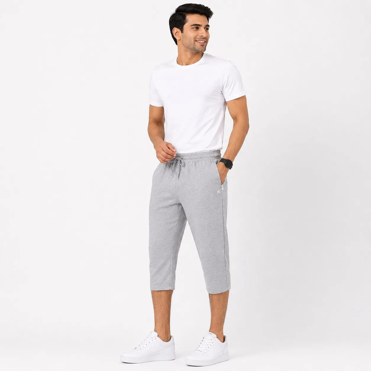 A man modeling a white crew-neck t-shirt and light gray heathered cropped sweatpants with a drawstring waist, paired with white sneakers, against a plain white studio background.