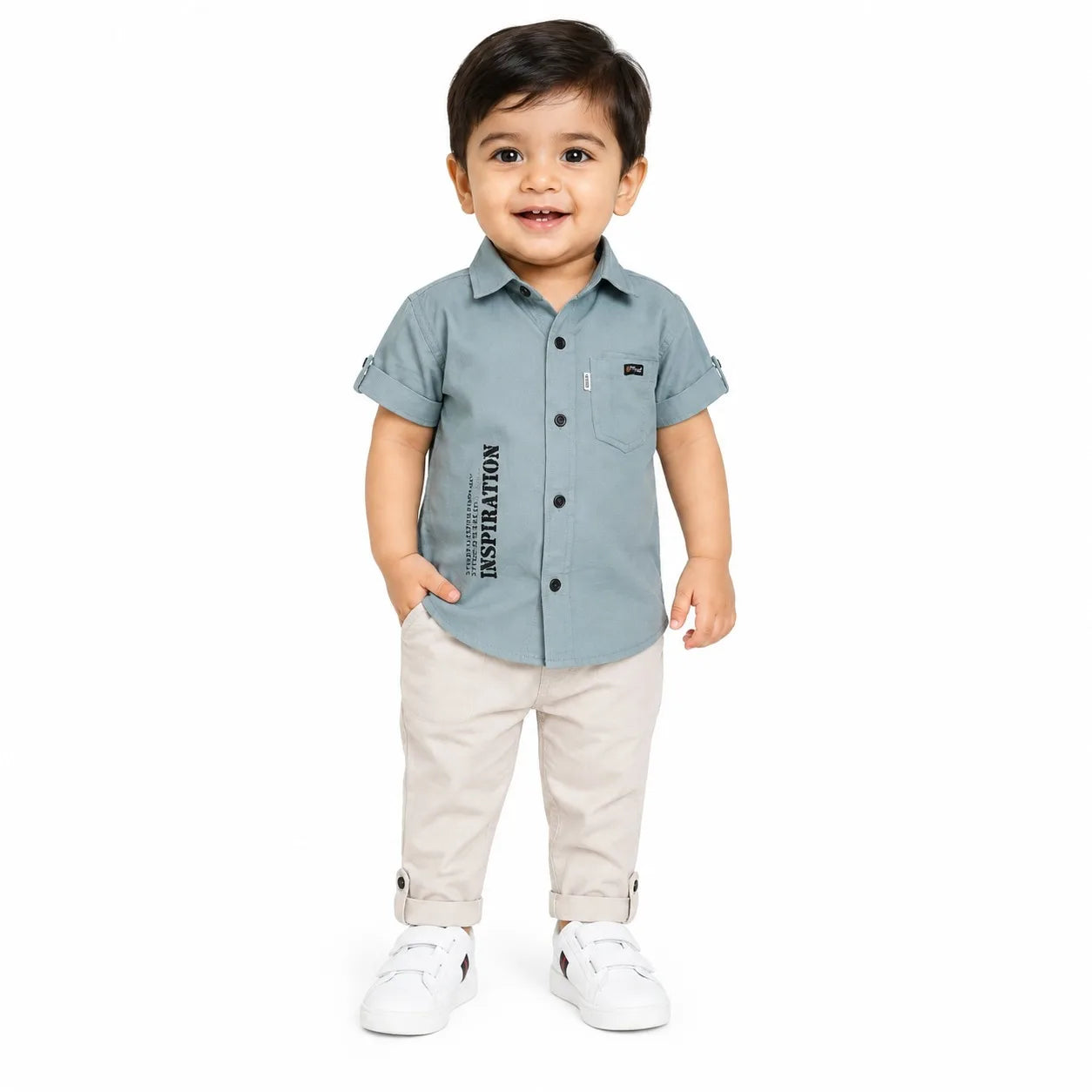 A toddler standing against a white background, wearing a light blue short-sleeve button-up shirt with vertical black text on the front pocket, beige pants, and white sneakers.