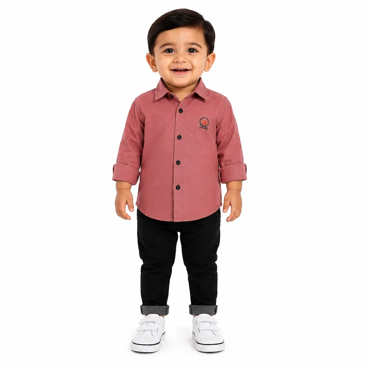 A toddler boy standing against a white background, wearing a dusty rose pink long-sleeve button-down shirt, black pants, and white sneakers.