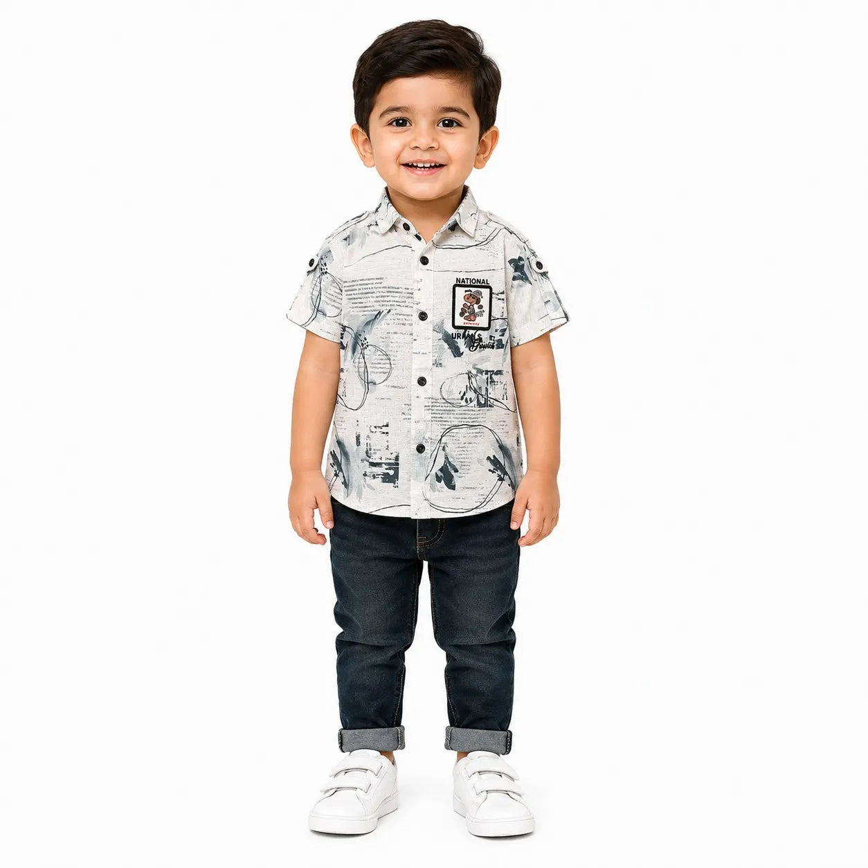 A young boy modeling a short-sleeve button-up shirt with a black and white graphic print, paired with dark blue jeans and white sneakers, set against a plain white background.