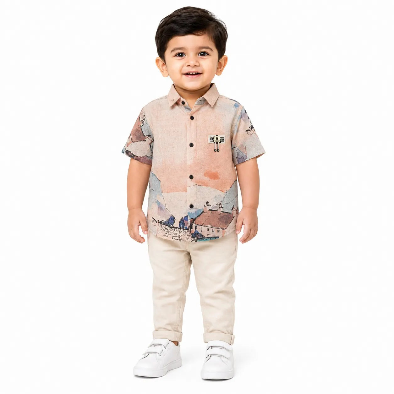 A toddler boy wearing a short-sleeve button-up shirt with a scenic landscape print in beige, orange, and blue, paired with beige pants and white sneakers, standing against a plain white background.