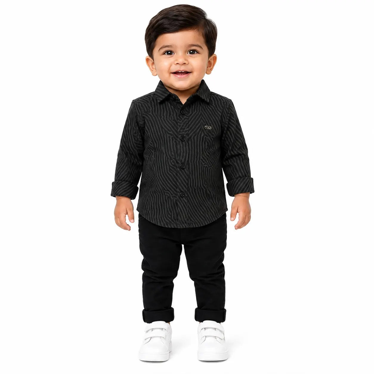 A toddler boy wearing a black and gray vertically striped long-sleeve button-up shirt, black pants, and white sneakers, standing against a solid white background.