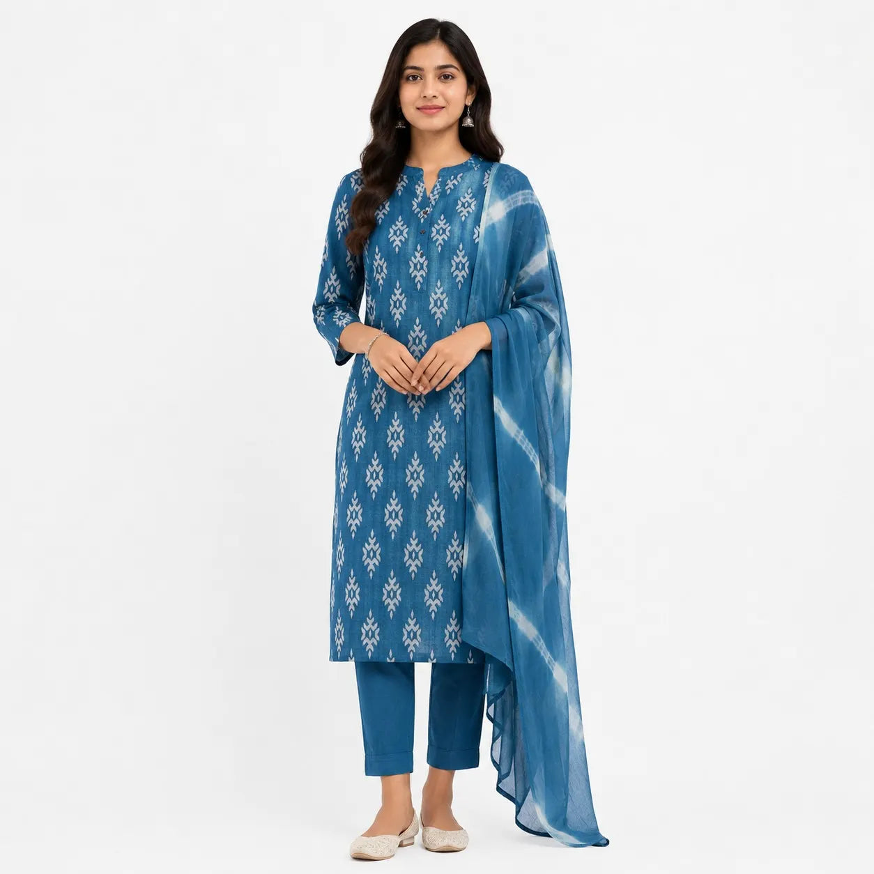 A woman modeling a blue three-piece traditional outfit with white geometric patterns, consisting of a long kurta, matching pants, and a sheer tie-dye dupatta, set against a plain white background.