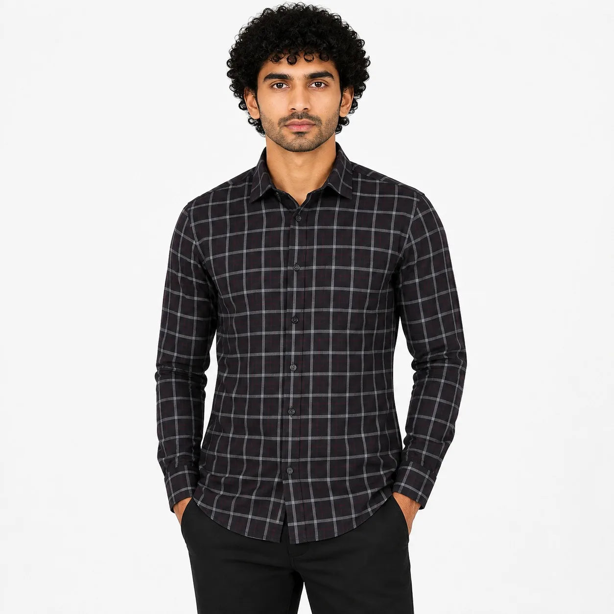A man wearing a black long-sleeve button-up shirt with a subtle gray and white windowpane plaid pattern, paired with black trousers, set against a plain white studio background.
