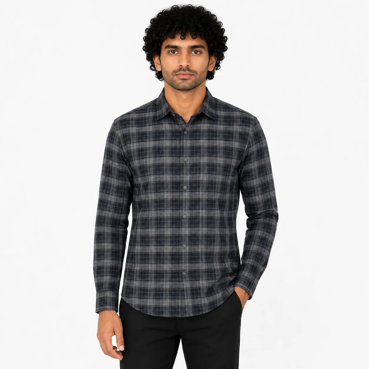 A man wearing a long-sleeve button-up plaid shirt in dark gray and black, paired with black pants, standing against a plain white background.